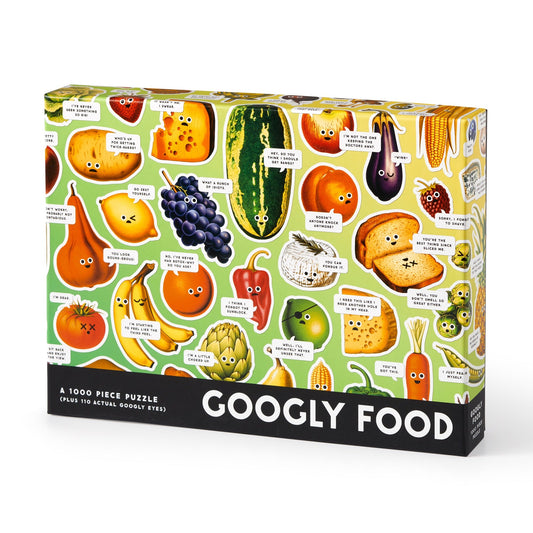 The Brass Monkey Googly Food 1000 Piece Puzzle features illustrated fruits and veggies with googly eyes and witty bubbles on a light green background. The box includes 1,000 pieces.