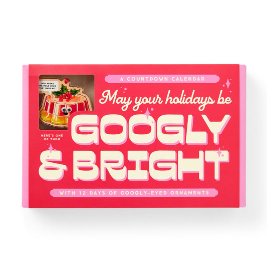 The Brass Monkey Googly & Bright Holiday Ornament Countdown Calendar features a pink box with “May your holidays be GOOGLY & BRIGHT” in bold letters, a clear window showing a googly-eyed ornament, and includes 12 days of festive surprises.