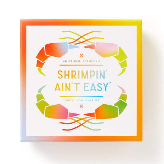 A vibrant box from Brass Monkey labeled Shrimpin Aint Easy Origami Kit features rainbow shrimp graphics and includes fun googly eyes for each folded shrimp creation.