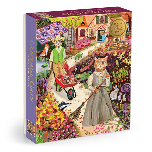 The Anja Riebensahm Cottage Cats 1000 Piece Foil Puzzle features a colorful scene of cats in vintage clothes tending to a cottage garden, with one cat pushing a wheelbarrow and another sweeping near flowers and a pink-roofed house.