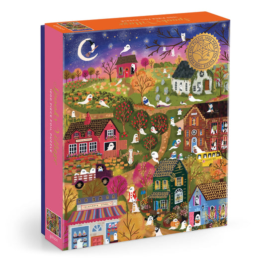 The Joy Laforme Spooky Village 1000 Piece Foil Puzzle features a vibrant nighttime scene with ghosts, pumpkins, orange-leaved trees, and a crescent moon on its box, plus a gold award seal in the top right corner.