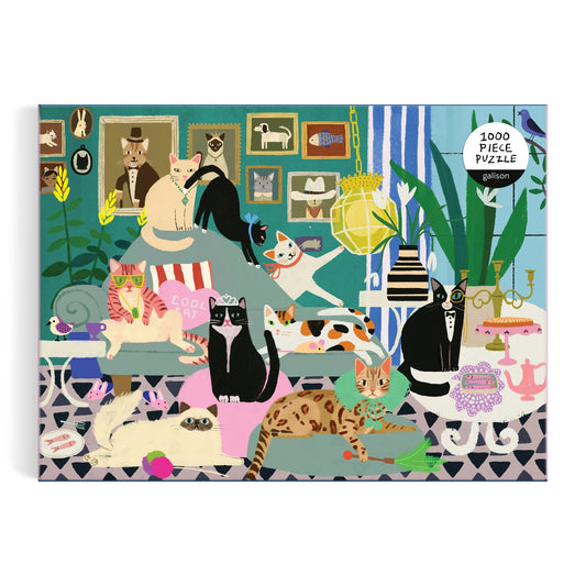 The Glamour Cats 1000 Piece Puzzle by Anne Bentley features a colorful illustration of glamorous cats relaxing and playing in a stylish living room decorated with plants, toys, and framed cat portraits.