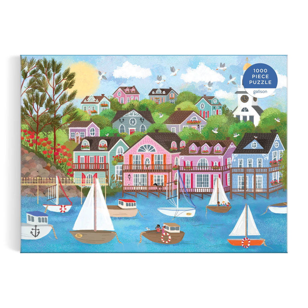 The Joy Laforme Harbor by the Sea 1000 Piece Puzzle features sailboats on a blue harbor, pastel houses, green trees, and a sunny sky—evoking Nantucket’s seaside charm. Box displays the puzzle name in the top right corner.