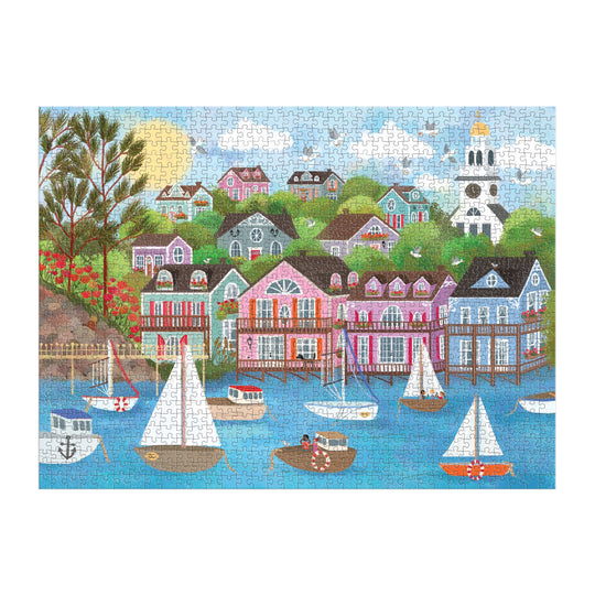 The Joy Laforme Harbor by the Sea 1000 Piece Puzzle features a vibrant Nantucket village with pastel hillside houses, a white clock-tower church, colorful sailboats on blue water, and trees beneath a sunny sky.