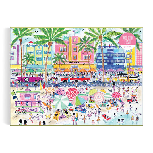 The Michael Storrings South Beach Miami 1000 Piece Puzzle by Michael Storrings features a vibrant illustrated box with sunbathers, umbrellas, palm trees, vintage cars, and Art Deco buildings in a lively beach scene.
