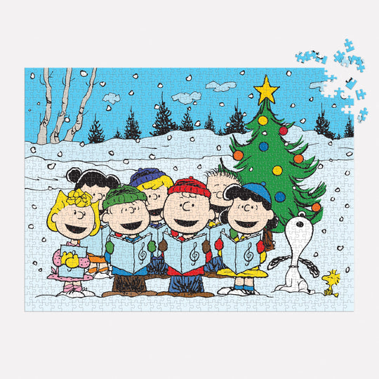The Peanuts Christmas Caroling 1000 Piece Puzzle by Peanuts Worldwide, LLC features beloved characters singing by a snowy tree with Snoopy and Woodstock. A few pieces are missing from the top right corner.
