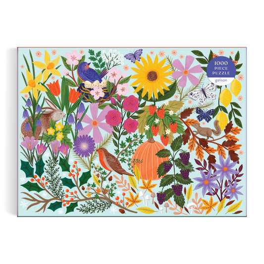The Lee Foster-Wilson “Seasons in Bloom” 1000 Piece Puzzle features a vibrant nature scene with flowers, birds, butterflies, berries, a pumpkin, and autumn leaves on a light background.