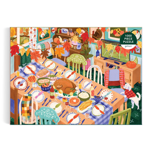 The Thankful Table 1000 Piece Puzzle by Carla Ellis features a festive dining scene with a large turkey, vibrant side dishes, autumn leaves decor, and a white dog by the table—all bathed in warm, welcoming light.