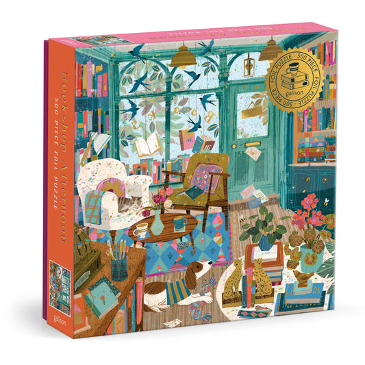 The Victoria Ball Bookshop Afternoon 500 Piece Foil Puzzle features a cozy bookstore scene with books, plants, cats, and birds. Large windows and bookshelves create a warm atmosphere—perfect for puzzlers and book lovers alike.