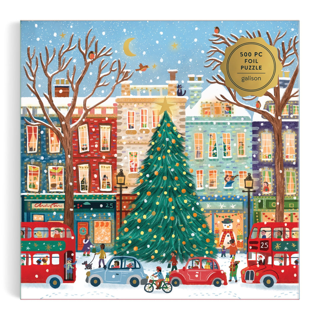 Illustrated winter street scene with a big decorated Christmas tree, bright buildings, people, buses, and snow. A gold label marks it as the Tinsel City 500 Piece Foil Puzzle by Laura Watkins—a festive urban holiday puzzle.