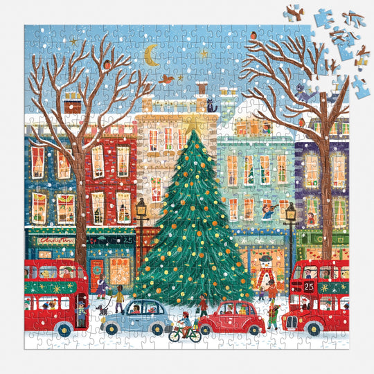 The Laura Watkins Tinsel City 500 Piece Foil Puzzle shows a festive city with a big Christmas tree, red double-decker buses, cars, bicyclists, and people in snowy streets. Several pieces are missing.