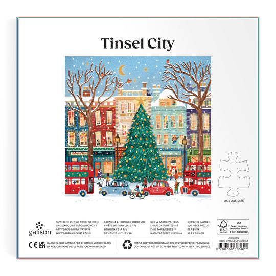 Illustration of a festive city with a big decorated Christmas tree, vibrant buildings, snow, people, and red double-decker buses under a starry sky features on the Tinsel City 500 Piece Foil Puzzle by Laura Watkins.