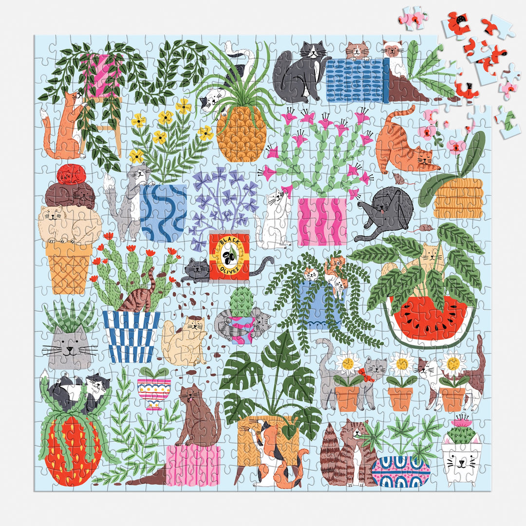 The Holly Maguire Cats in the Houseplants 500 Piece Puzzle features playful cats among houseplants, pineapples, and watermelons on a light blue background with a few pieces unplaced in the upper right corner.
