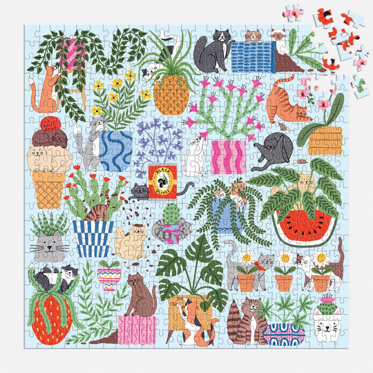 The Holly Maguire Cats in the Houseplants 500 Piece Puzzle features playful cats among houseplants, pineapples, and watermelons on a light blue background with a few pieces unplaced in the upper right corner.
