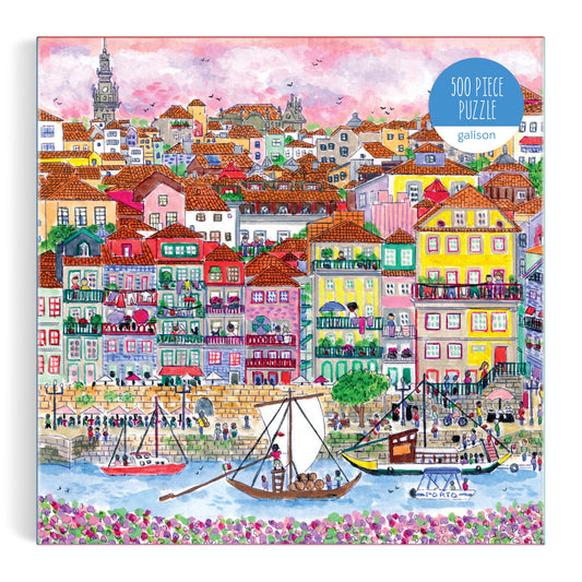 The Michael Storrings Colors of Porto 500 Piece Puzzle by Michael Storrings features a colorful illustrated harbor scene with boats, people on the waterfront, and vibrant hillside houses under a pink and purple sky.