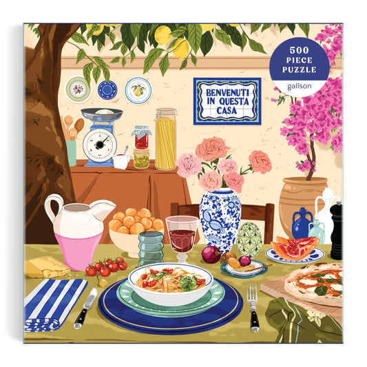 Enjoy Ana Hards Tuscan Afternoon 500 Piece Puzzle, featuring a vibrant Italian meal with pasta, bread, fruit, wine, and flowers on a table. Kitchen items and a “Benvenuti in questa casa” sign complete this perfect Italian food-themed puzzle.