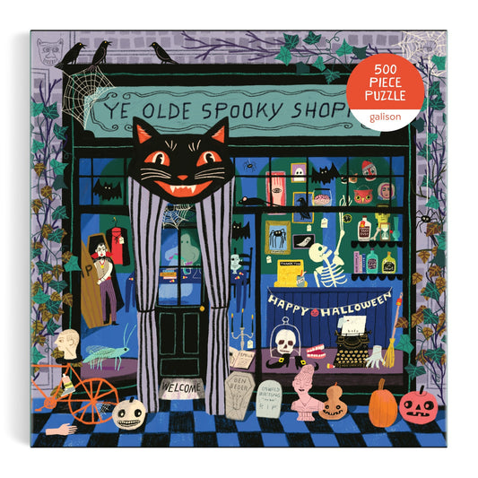 Ye Olde Spooky Shoppe 500 Piece Puzzle by Anne Bentley features a vibrant Halloween-themed storefront with a black cat sign, skeletons, pumpkins, potions, cobwebs, spooky decorations, and a Happy Halloween banner.