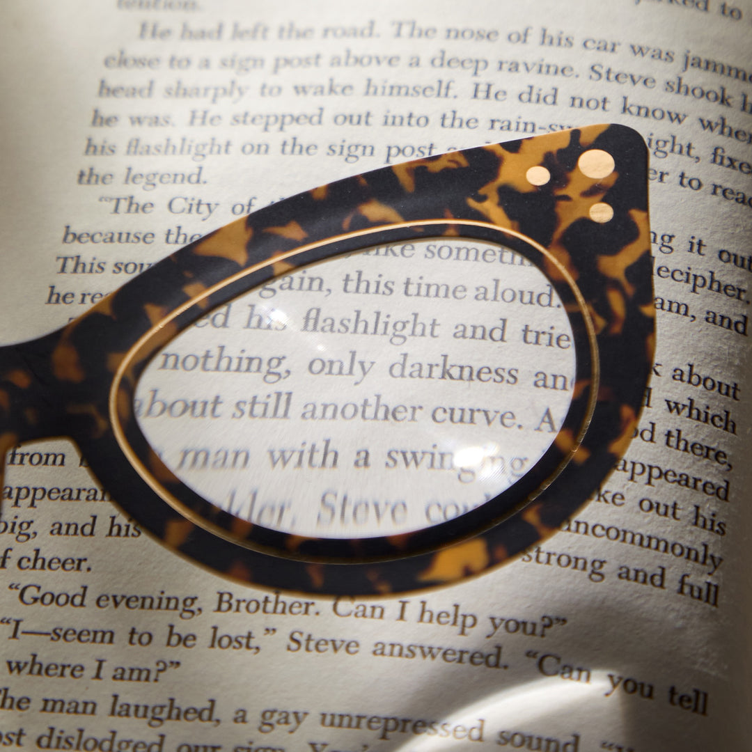 Galisons Cat Eye Readers Bookmark with Magnifier rests on an open book, its lens clearly magnifying the printed text for easy reading.