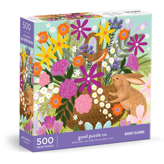 The Good Puzzle Co. Basket Blooms 500pc Puzzle by Lee Foster-Wilson features a vibrant illustration of a rabbit and bird among flowers in a woven basket. Made from recycled materials, this colorful puzzle is sure to delight.