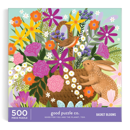 The Good Puzzle Co. Basket Blooms 500pc Puzzle by Lee Foster-Wilson features a rabbit and bird in a vibrant basket of daisies, pink roses, and purple flowers—a delightful holiday challenge for all ages.