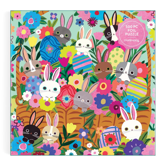 Charming cover art by Tara Lilly features bunnies with big eyes among Easter eggs and flowers, set against green leaves. This illustration appears on the Blooming Bunnies 500 Piece Foil Family Puzzle.