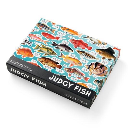The Judgy Fish 1000 Piece Puzzle by Brass Monkey features colorful illustrated fish on a bright blue background, uses recycled materials, and displays fish names in bold black and white text.