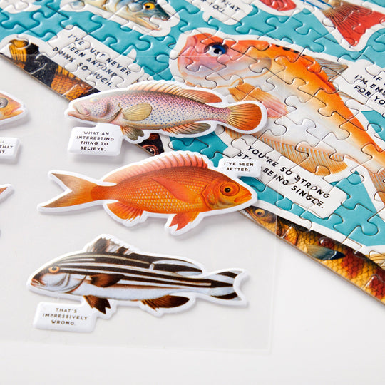 A close-up of Brass Monkeys Judgy Fish 1000 Piece Puzzle, a colorful spot UV puzzle where each fish has a humorous speech bubble like “I’ve seen better” and “That’s impressively wrong.”.