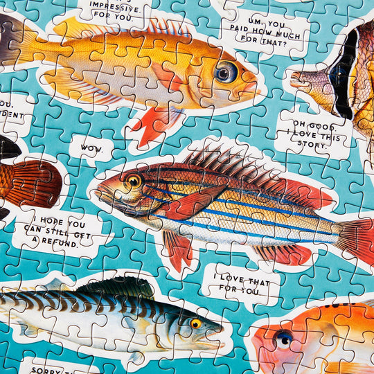 The Judgy Fish 1000 Piece Puzzle by Brass Monkey is a colorful spot UV puzzle with illustrated fish making witty remarks on a blue background, crafted from recycled materials.
