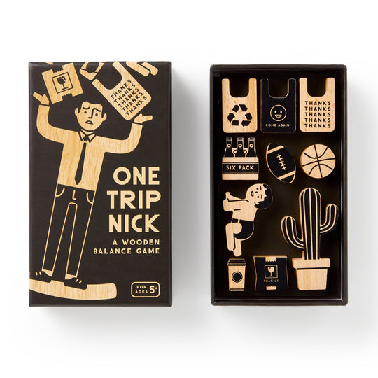 The Brass Monkey One Trip Nick Wooden Balance Game features a worried cartoon man on the box carrying groceries. Inside are wooden game pieces shaped like groceries, a cactus, a ball, a drink, a bag, and a baby.