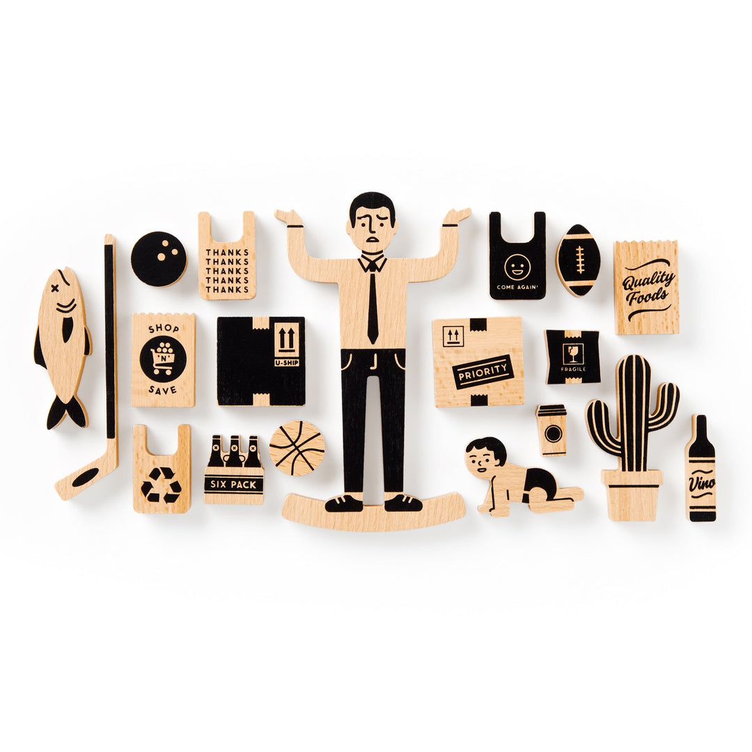 The Brass Monkey One Trip Nick Wooden Balance Game features grocery-themed wooden pieces like shopping bags and a wine bottle, plus fun shapes such as a man shrugging, fish, basketball, recycling symbol, baby crawling, cactus, and more.