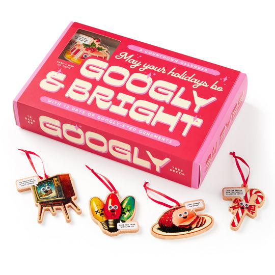 The Brass Monkey Googly & Bright Holiday Ornament Countdown Calendar features four quirky googly-eyed ornaments—a retro TV, Christmas lights, a sushi roll, and a candy cane—each with a red ribbon in a pink box.