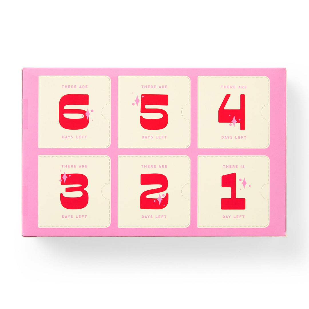 The Brass Monkey Googly & Bright Holiday Ornament Countdown Calendar features six numbered pink compartments, each with bold red digits on cream, perfect for building holiday excitement or storing small ornaments.