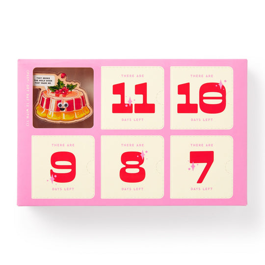 The Brass Monkey Googly & Bright Holiday Ornament Countdown Calendar is a pink box with six sections showing 11 to 7 days left in bold red. A cartoon jelly dessert with googly eyes and a sign, Its grown on me, decorates the top left.