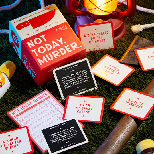 Brass Monkey’s Not Today, Murder Game is displayed on grass with its game cards, scorecard, lantern, plastic axe, honey bear bottle, and various props arranged around the game box.