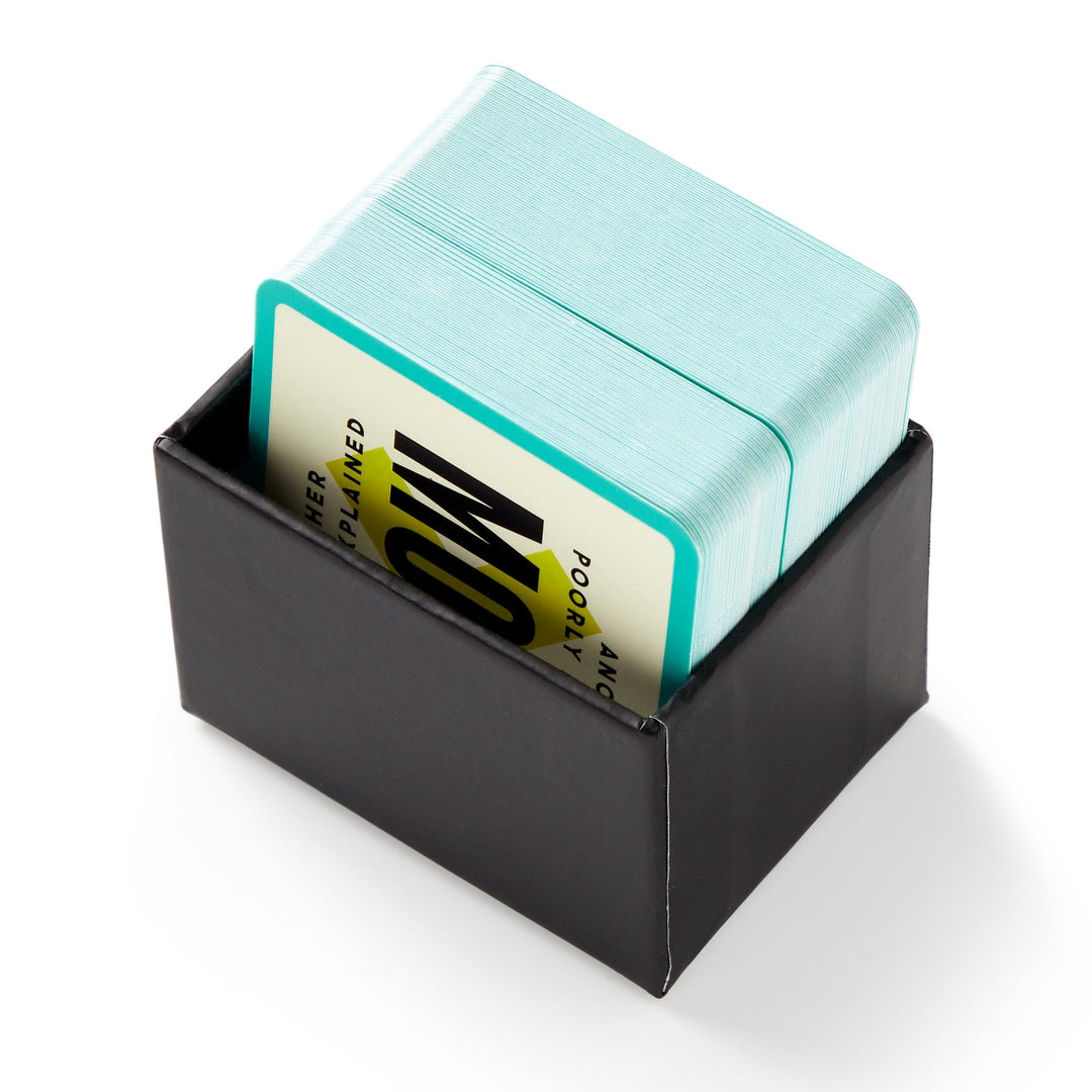 A black box holds Brass Monkey’s Mini Poorly Explained Movies - 80s Edition, a stack of turquoise-edged cards ideal for party games, with the top card showing bold black text on a yellow and white background.
