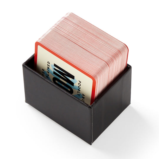 Mini Poorly Explained Movies - Holiday Edition by Brass Monkey features a stack of red-edged playing cards in a sleek black box, perfect for holiday movie nights. The top card shows bold black text on a blue and white background.