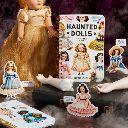 Brass Monkeys Haunted Dolls Sticker Book, featuring a doll in a yellow dress and oversized doll limbs, is arranged in smoky mist atop dark books—creating an eerily perfect scene for ghostly friends.