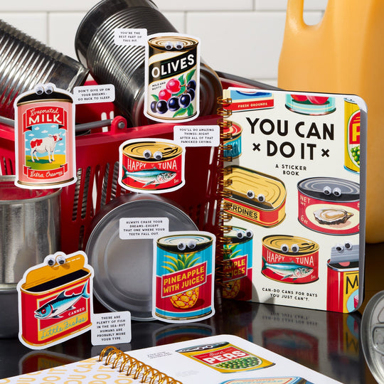 A vibrant Brass Monkey display features the You Can Do It Googly Sticker Book, playful can-shaped cards, and retro kitchen-themed items like metal pots and a yellow kettle—all adorned with googly eyes for extra charm.