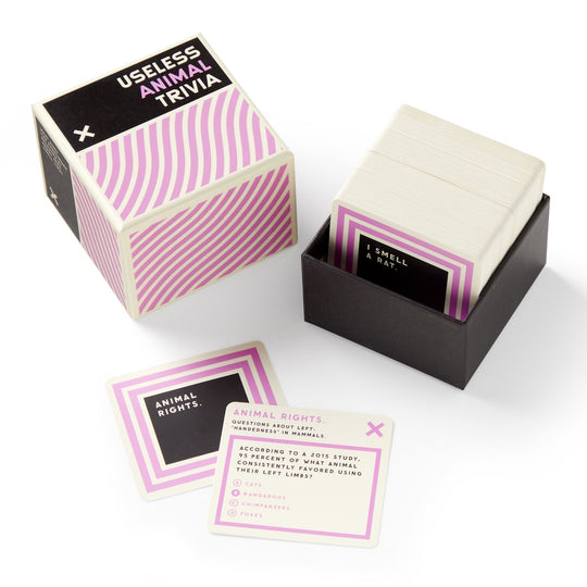 An open box of Brass Monkey’s Useless Animal Trivia reveals a stack of black, white, and purple cards. Two cards are shown featuring quirky animal facts and animal rights questions.