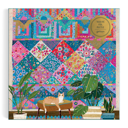 The Victoria Ball Quilter’s Corner 1000 Piece Foil Puzzle by Victoria Ball features a cat on a table with potted plants, set before a vibrant pink, blue, and purple patterned quilt. A gold foil sticker highlights the 1000 piece count.