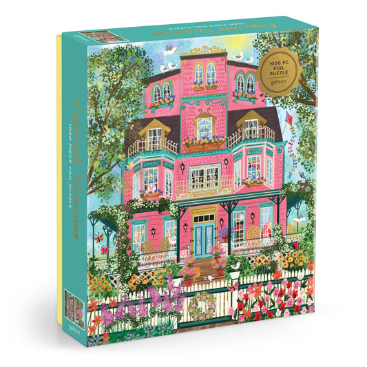 The Joy Laforme Capeside Victorian 1000 Piece Foil Puzzle features a whimsical pink Victorian mansion with balconies, blooming flowers, trees, a white fence, and birds on the roof in a vibrant outdoor scene.