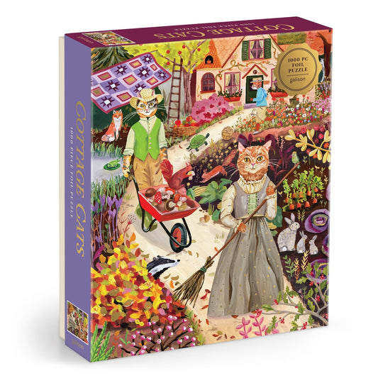 The Anja Riebensahm Cottage Cats 1000 Piece Foil Puzzle features a colorful scene of cats in vintage clothes tending to a cottage garden, with one cat pushing a wheelbarrow and another sweeping near flowers and a pink-roofed house.
