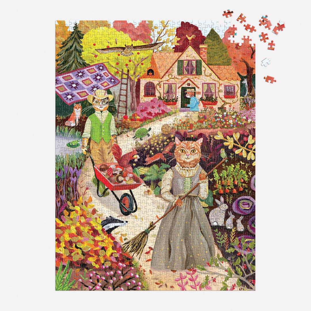 The Cottage Cats 1000 Piece Foil Puzzle by Anja Riebensahm features a colorful garden with two vintage-clad cats gardening, a woman by a cottage, and a patchwork quilt outside. Several puzzle pieces are missing from the top right corner.