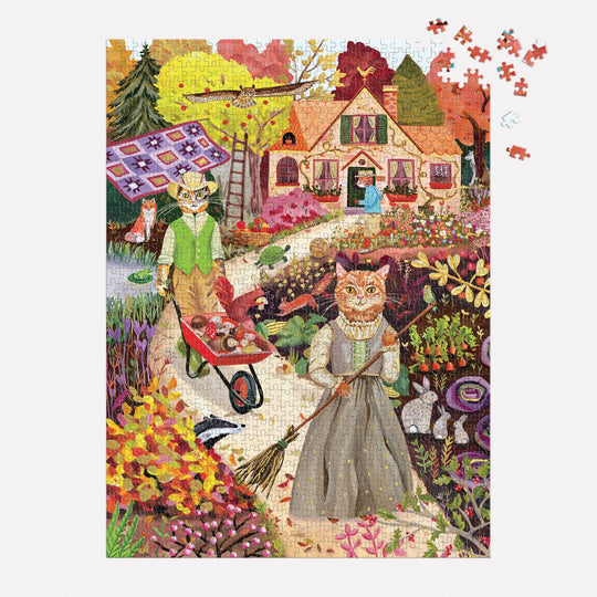 The Cottage Cats 1000 Piece Foil Puzzle by Anja Riebensahm features a colorful garden with two vintage-clad cats gardening, a woman by a cottage, and a patchwork quilt outside. Several puzzle pieces are missing from the top right corner.
