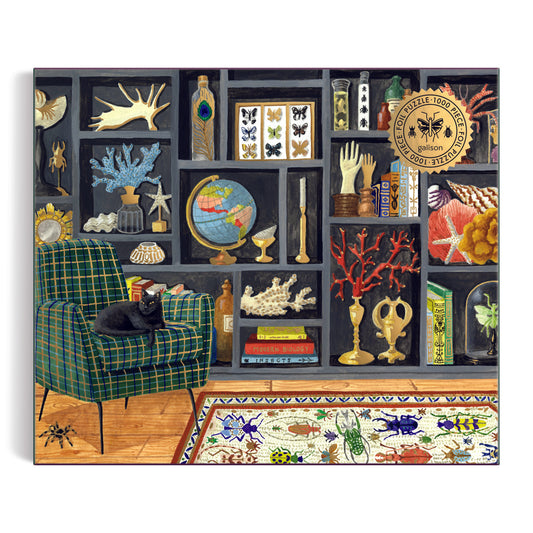A black cat rests on a green plaid chair before shelves of globes, coral, and butterflies, with an ornate insect rug—evoking the Mélanie Voituriez Eclectic Treasures 1000 Piece Foil Puzzle’s charm.