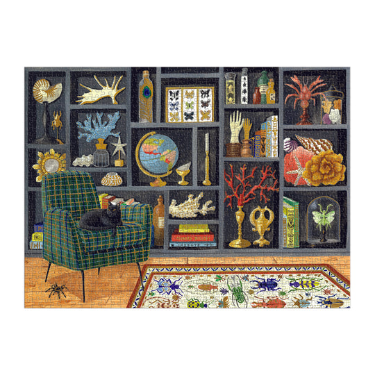 A bookshelf filled with globes, seashells, books, and curiosities stands behind a green plaid armchair with a black cat. A floral rug covers the floor—just like the Mélanie Voituriez Eclectic Treasures 1000 Piece Foil Puzzle.