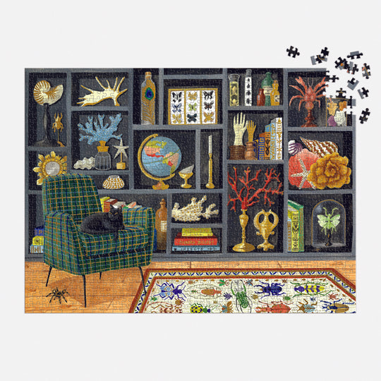 A nearly completed Eclectic Treasures 1000 Piece Foil Puzzle by Mélanie Voituriez shows a black cat dozing on a plaid armchair in a cozy study. Just a few precision-cut pieces are left to finish the inviting top right corner of the artwork.