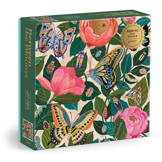 The Christine De Carvalho "Between the Blooms" 1000 Piece Foil Puzzle features colorful butterflies and pink flowers with green leaves on a cream background, with its title displayed on the box side.
