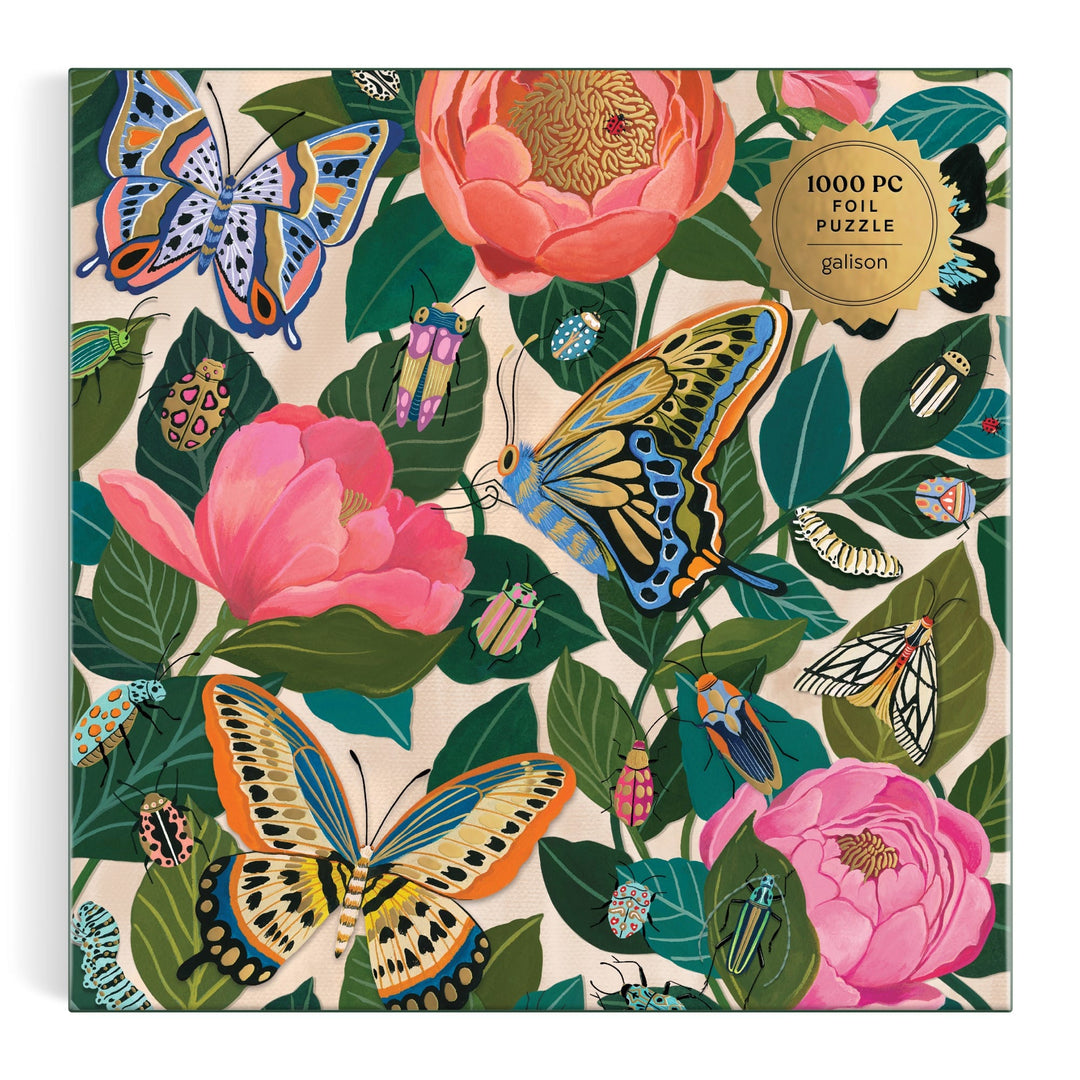 The Between the Blooms 1000 Piece Foil Puzzle by Christine De Carvalho features butterflies, beetles, and moths among pink flowers and green leaves, with a gold label that reads “1000 piece foil puzzle.”.