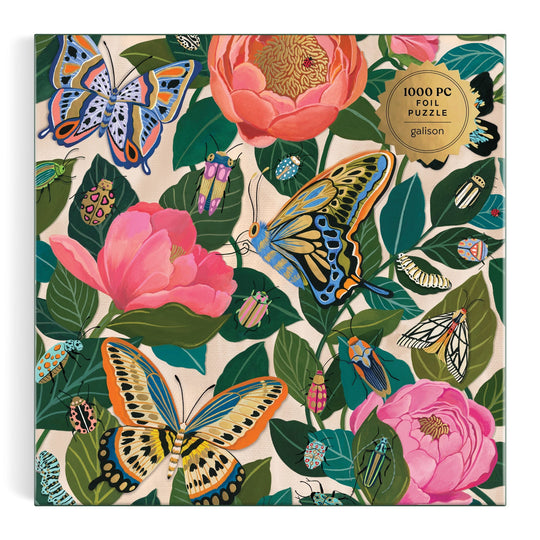 The Between the Blooms 1000 Piece Foil Puzzle by Christine De Carvalho features butterflies, beetles, and moths among pink flowers and green leaves, with a gold label that reads “1000 piece foil puzzle.”.